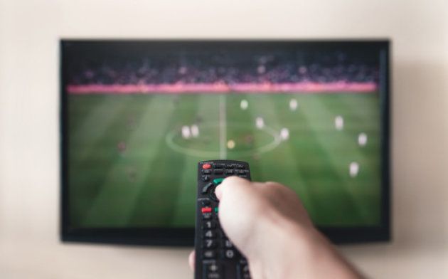 Human hand holding remote control at TV screen