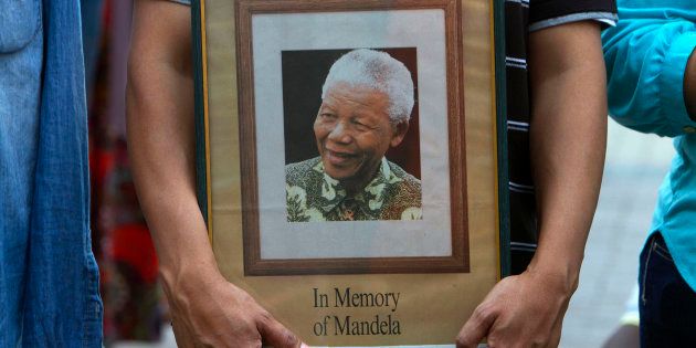 A man holds a tribute photograph as he watches the funeral service for former South African President Nelson Mandela on a large screen television in Cape Town, December 15, 2013.