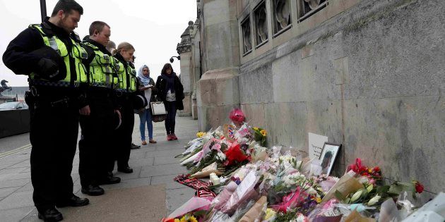 Police officers and civilians look at floral tributes near Westminster Bridge following a recent attack in Westminster, in London, Britain March 24, 2017.