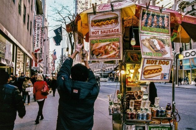 A hot dog cart vendor screws in a new lightbulb on to his fast food cart on 5th Avenue in Manhattan, New York.