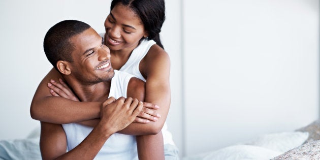 Shot of a woman hugging her husband from behind while sitting on their bed