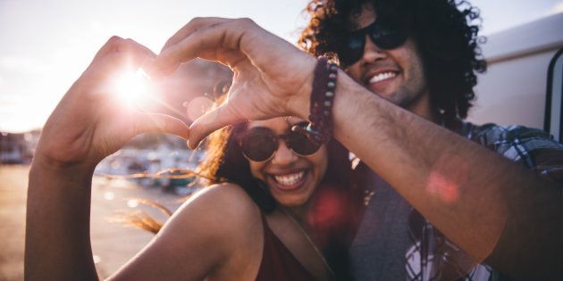 Happy young hipster couple making heart shape with hands close to a vintage van during a summertime road trip