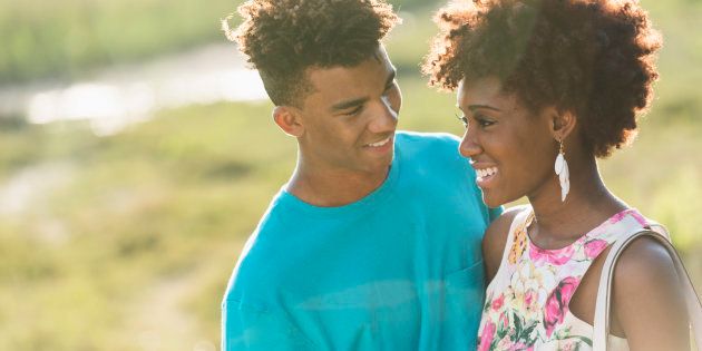 Close up portrait of a happy African American couple standing together outdoors on a sunny, summer day, face to face. The young woman is wearing a floral, sleeveless dress. Her boyfriend is wearing blue t-shirt.