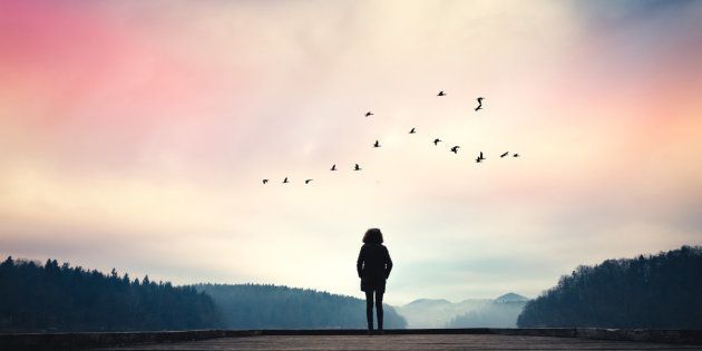 Woman standing on jetty and watching sunrise by the lake.