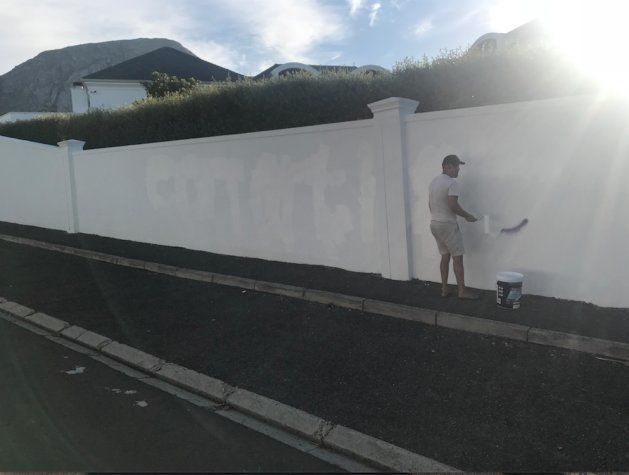 A painter is seen trying to cover the words "con artist" outside the home of ex Steinhoff CEO Markus Jooste
