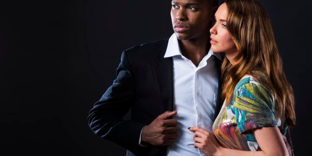 Mixed race couple in fashionable clothing posing in studio on black background, horizontal photo with copy space.