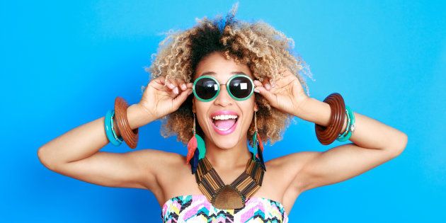 Summer portrait of happy afro american young woman wearing summer clothes and sunglesses, standing against blue background and laughing at camera.