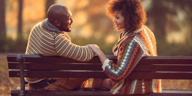 Loving African American couple talking to each other while sitting on bench in autumn park.
