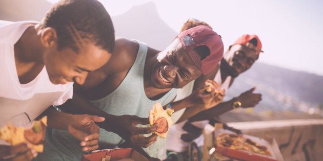 Group of adolescent friends laughing while happily sharing pizza