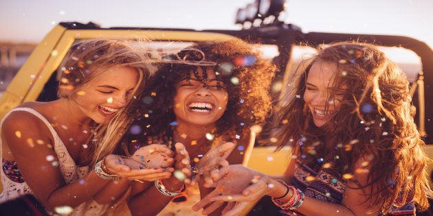 Afro girl and her friends on a road trip together blowing colourful confetti