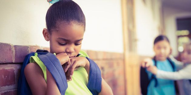 Sad pupil being bullied by classmates at corridor in school