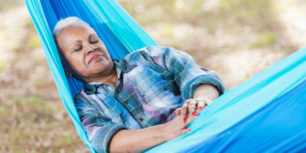 A senior African American woman asleep in a blue hammock.