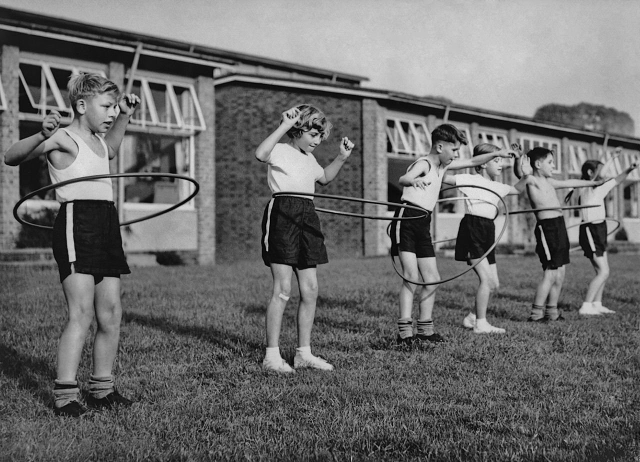 A group of six children play with hoops in a circa-1960s hoop class.