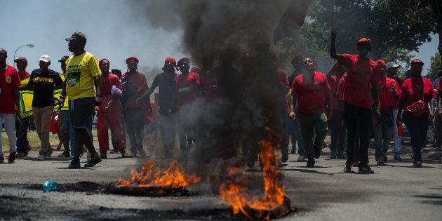 Protesters, including disgruntled parents, South African ruling Party African National Congress supporters, South African opposition party Economic Freedom Fighters supporters and members march near burning tyres during clashes with South African riot police officers during unrest over language and admission policies at Ho'rskool (Hoerskool) Overvaal school on January 17, 2017 in Vereeniging, South Africa. / AFP PHOTO / MUJAHID SAFODIEN (Photo credit should read MUJAHID SAFODIEN/AFP/Getty Images)