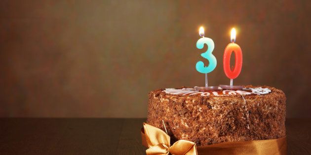 Birthday chocolate cake with burning candles as a number thirty on brown background