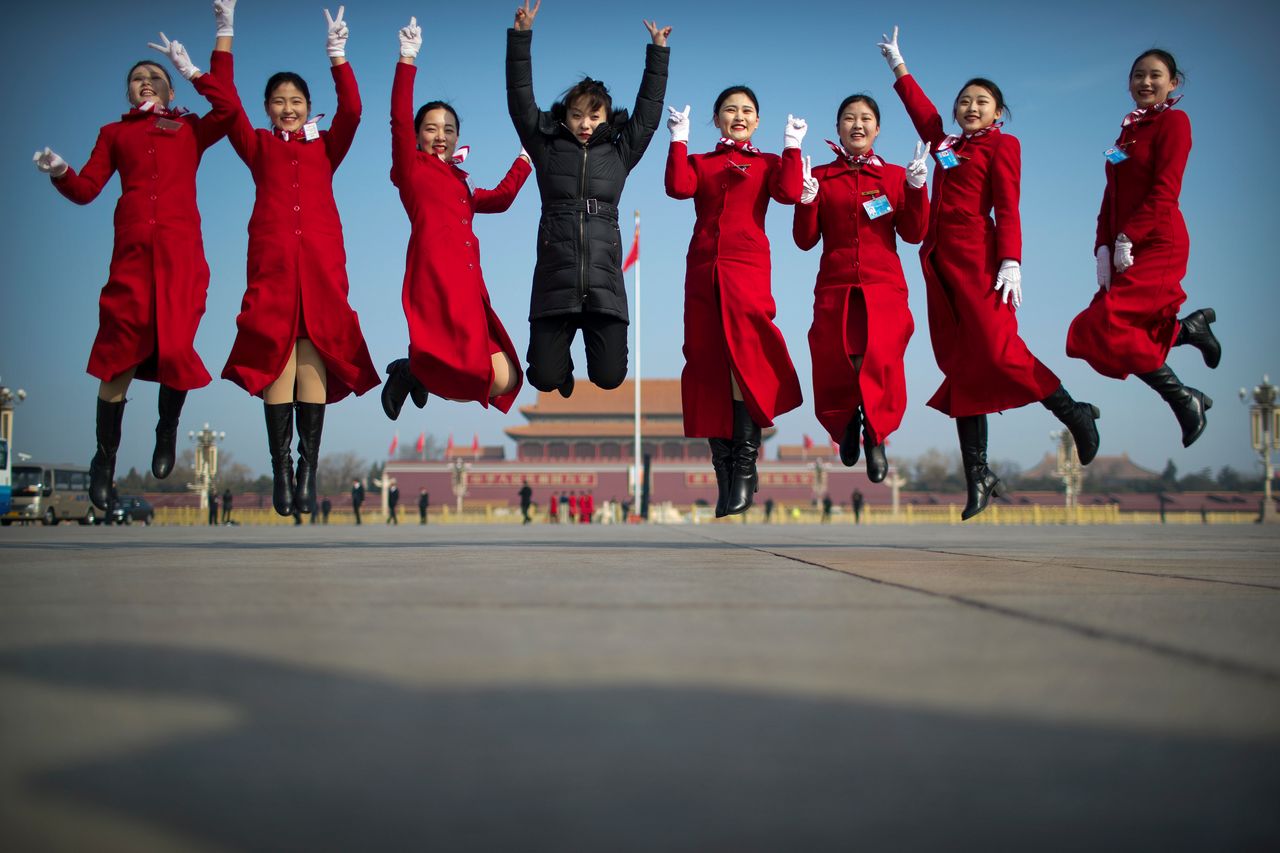 In this March 4, 2019, photo, bus ushers leap as they pose for a group photo during a meeting one day ahead of the opening session of China's National People's Congress (NPC) at the Great Hall of the People in Beijing. A year since removing any legal barrier to remaining China's leader for life, Xi Jinping appears firmly in charge, despite a slowing economy, an ongoing trade war with the U.S. and rumbles of discontent over his concentration of power.