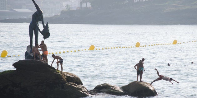 Bañistas en Sansenxo, junto a la escultura 'La madama de Silgar', de Alfonoso Vilar Lamelas.