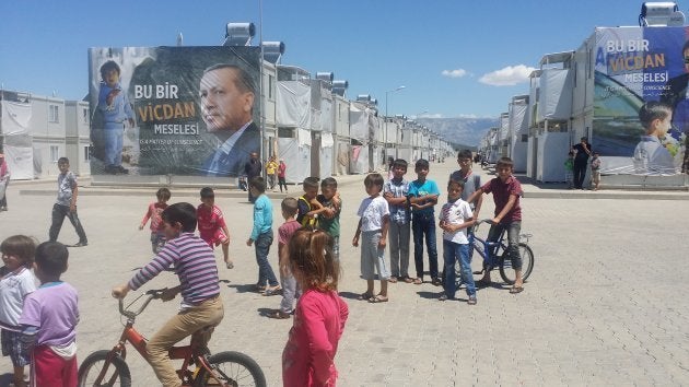 Niños refugiados miran y juegan. El cartel de atrás representa a un angustiado niño frente a Erdoğan, presidente de Turquía, bajo el lema: "es una cuestión de conciencia". | Campo de Kahramanmaraş.