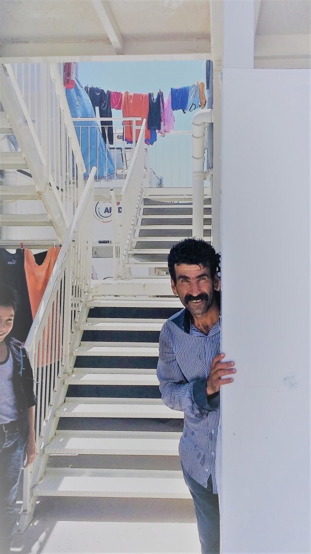 Un hombre se asoma a la puerta de su unidad de alojamiento. Los refugiados pueden salir de los campos para encontrar trabajo y establecerse en ciudades vecinas. | Campo de Osmaniye.