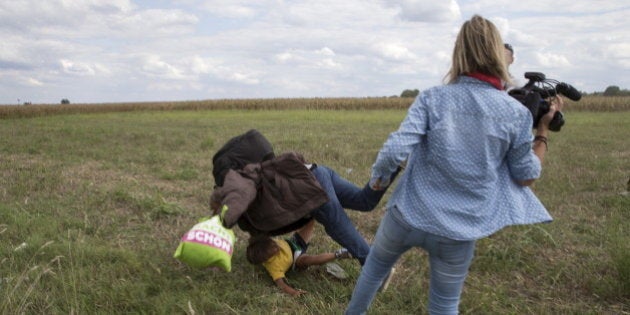 A migrant carrying a child falls after tripping on TV camerawoman (R) Petra Laszlo while trying to escape from a collection point in Roszke village, Hungary, September 8, 2015. Laszlo, a camerawoman for a private television channel in Hungary, was fired late on Tuesday after videos of her kicking and tripping up migrants fleeing police, including a man carrying a child, spread in the media and on the internet. REUTERS/Marko Djurica