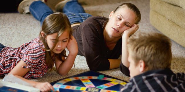 A mother nods off to sleep as her two children go on playing a board game.
