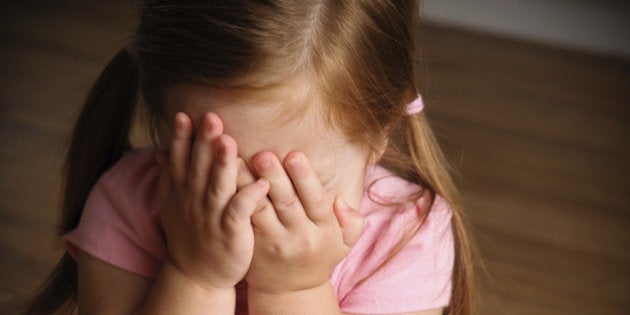 Color image of two year old red-haired girl covering her eyes.