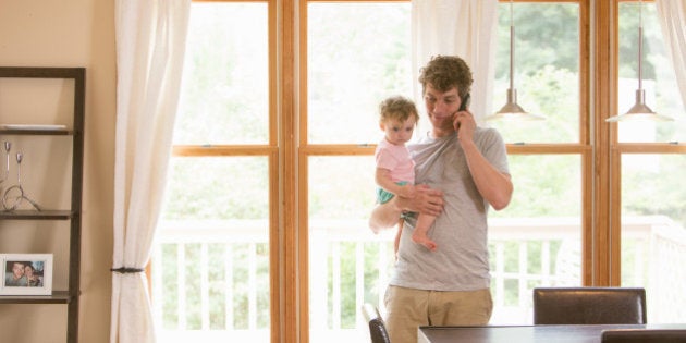Father holding 1 year old daughter while talking on phone in domestic home