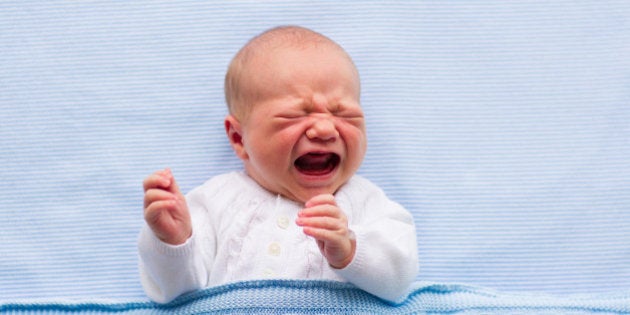 Newborn crying baby boy. New born child tired and hungry in bed under blue knitted blanket. Children cry. Bedding for kids. Infant screaming. Healthy little kid shortly after birth. Cable knit textile