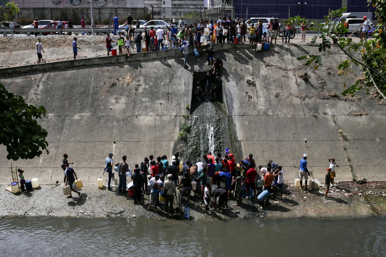 Venezuelans collect water flowing into a sewage canal from a broken pipe at the Guaire River in Caracas on March 11, 2019, as a massive power outage continues affecting some areas of the country amid a longstanding political crisis. 
