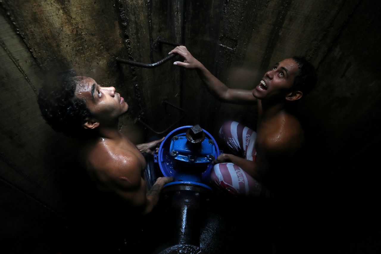 Locals collect water from an underground water main pipeline in Caracas, Venezuela, on March 12, 2019.