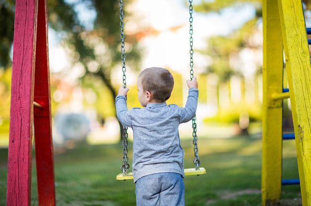 Blond boy swinging on the playground,rear view