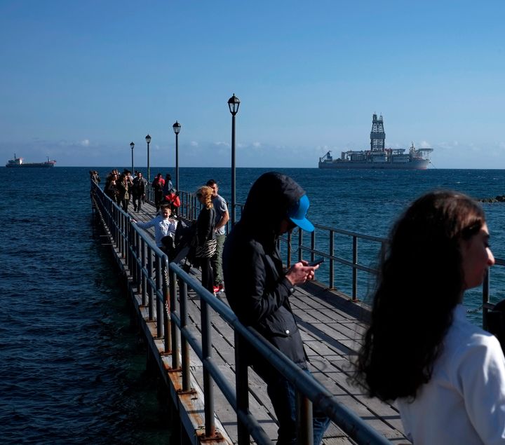 Κύπριοι νέοι σε αποβάθρα της Λεμεσού και στο βάθος ένα πλοίο - γεωτρύπανο, από αυτά που παίρνουν μέρος στις έρευνες.