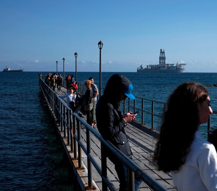 Κύπριοι νέοι σε αποβάθρα της Λεμεσού και στο βάθος ένα πλοίο - γεωτρύπανο, από αυτά που παίρνουν μέρος στις έρευνες.