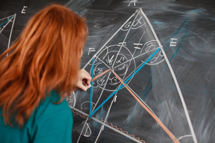 pretty young college student writing on the chalkboard/blackboard during a math class (color toned image; shallow DOF)