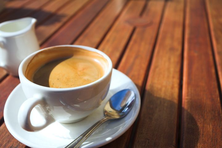A cup of coffee on a wooden table in an outdoor cafe. Shallow depth of field, focus on the rim of the cup
