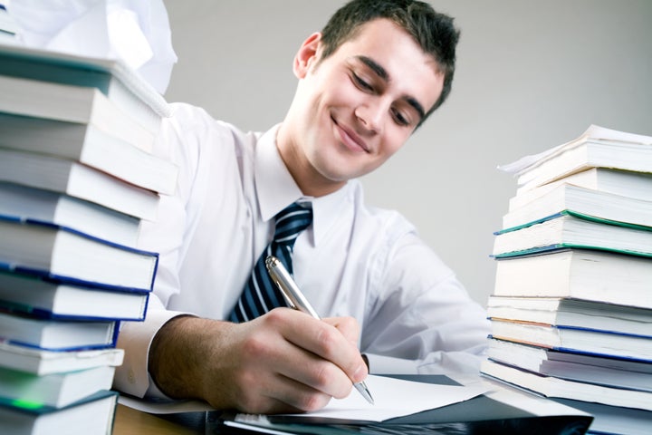 Young student writing something on the paper sheet, smiling. Focus on the hand with a pen.