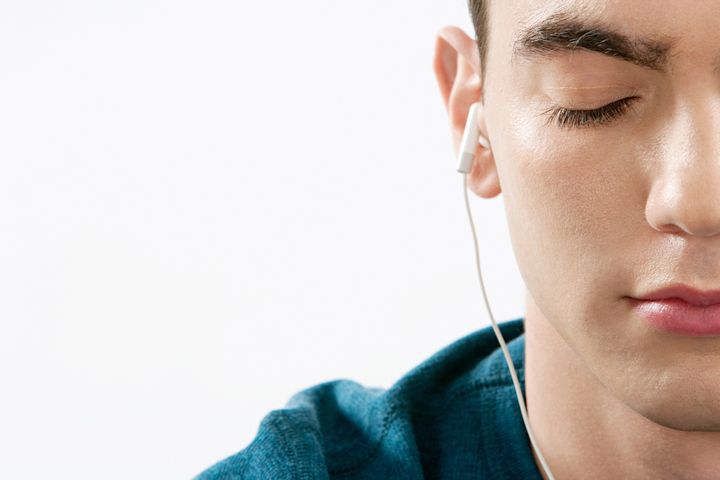 Close up portrait of a teenager's half face closing his eyes while listening to music with his headphones against a white background.