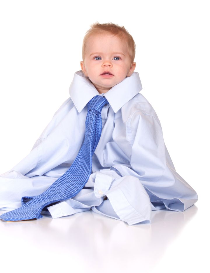 An image of a cute baby in a suit, wearing over sized clothes. Images is isolated on white with reflection.