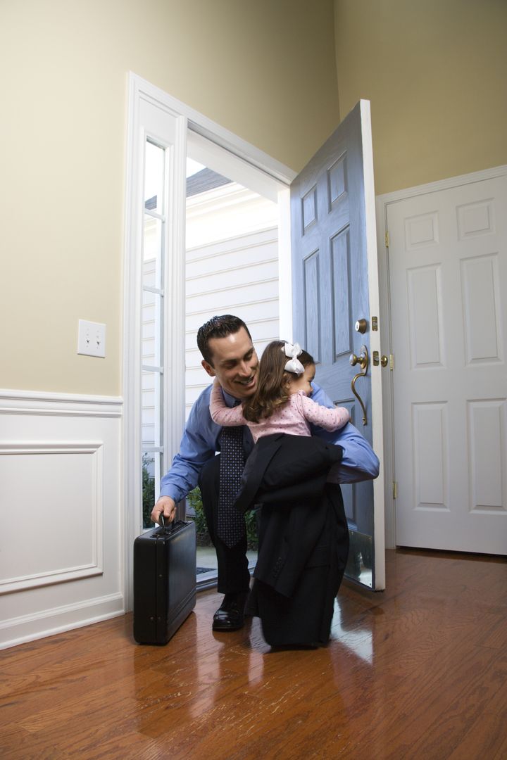 Caucasian businessman at open door with briefcase hugging daughter.