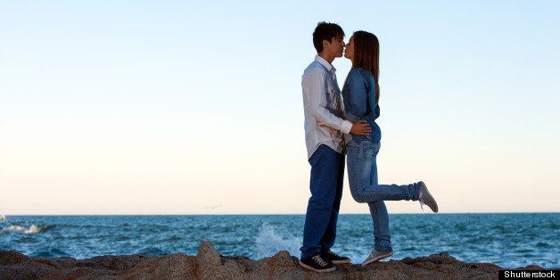 Romantic couple kissing on rocks at seaside.