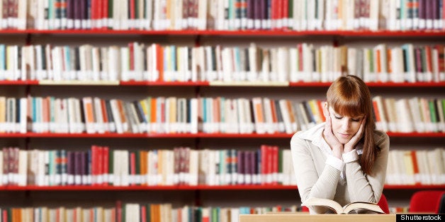 Portrait of a serious young student reading a book in a library