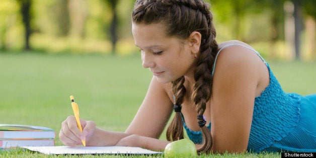 Young beautiful girl writing into her notebook in the park