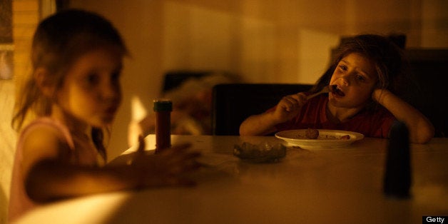 SEVILLE, SPAIN - JUNE 01: Five-year-old twin sisters Kiomara Laguna Arias (R) and Tatiana, who were evicted from their home with their parents and brother, eat their dinner lit by the yellow street lights after electricity was cut off, at their apartment, which is part of a complex occupied by the Corrala Utopia community on June 1, 2013 in Seville, Spain. In 2010 Spanish banks foreclosed more than 100,000 households which contributed to the already large number of empty houses. With as many as one million properties unsold, victims of Spain's financial crisis, struggling to keep a roof over their head due to high levels of unemployment and severe cuts to social welfare, have turned to squatting in the empty buildings. The Corrala Utopia is a community, on a steadily growing list of communities all over Spain, living in squatted buildings. In this case the building stood empty for three years before the squatters moved in almost a year ago. The community houses a total of 36 families including almost 40 children. The families are cut off from water and electricity and live with an uncertain future and the fear of being evicted soon again. For the first time in history over 6 million Spaniards are jobless in Spain, the euro zone's fourth-biggest economy. (Photo by Jasper Juinen/Getty Images)