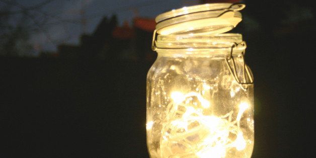 A vintage jar of small glowing lights at night time in the garden.