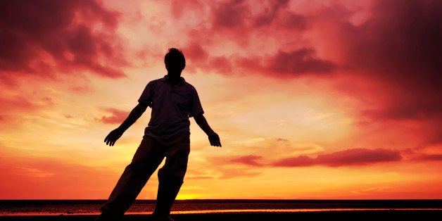 Senior man performing Chinese Tai Chi Kung Fu under sunset at beach.