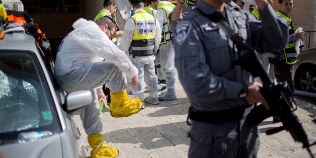 israeli police officer and Israeli rescue workers work at the scene of a shooting attack in a Synagogue in Jerusalem, Tuesday, Nov. 18, 2014. Two Palestinians stormed a Jerusalem synagogue on Tuesday, attacking worshippers praying inside with knives, axes and guns, and killing four people before they were killed in a shootout with police, officials said. (AP Photo/Ariel Schalit)