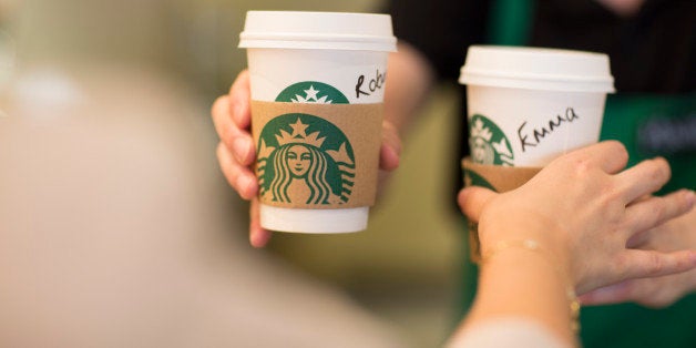 An employee, right, hands a customer personalised cardboard coffee cups inside a Starbucks Corp. coffee shop in London, U.K., on Monday, June 9, 2014. U.K. services companies' confidence rose to a record this quarter, indicating continued expansion in the largest part of the economy, the Confederation of British Industry said. Photographer: Jason Alden/Bloomberg via Getty Images