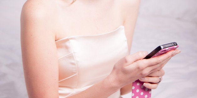 Beautiful young woman ready to go out to a ball, a prom or could be a bridesmaid. She is milling and looking, texting on her smart phone while sitting on her bed