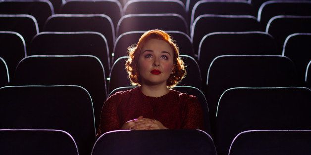 A beautiful young woman with red hair sits alone in a cinema.