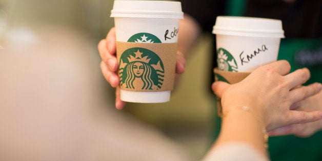 An employee, right, hands a customer personalised cardboard coffee cups inside a Starbucks Corp. coffee shop in London, U.K., on Monday, June 9, 2014. U.K. services companies' confidence rose to a record this quarter, indicating continued expansion in the largest part of the economy, the Confederation of British Industry said. Photographer: Jason Alden/Bloomberg via Getty Images